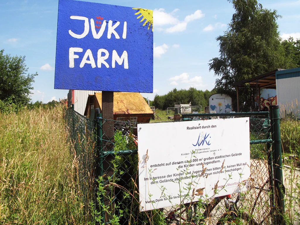 Selbst gemaltes Schild mit der Aufschrift „JuKi Farm“ an einem Zaun.